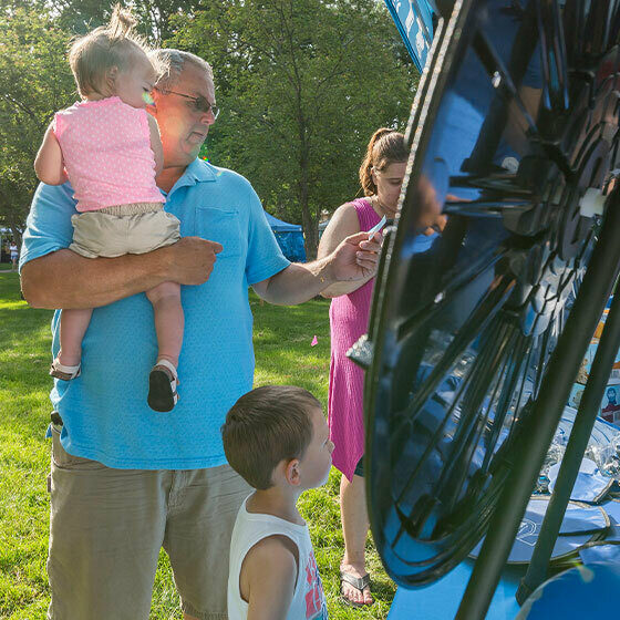 A man holding his daughter while his young son watches him spin the prize wheel at the blue ribbon classics booth during Ice Cream Days in Le Mars.