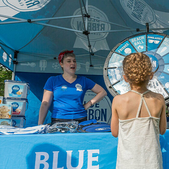 A blue ribbon classics booth attendant talking to a little girl at the blue ribbon booth during ice cream days in le mars.