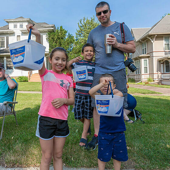 a man and his three young kids holding up their prize buckets to the camera during ice cream days at le mars.