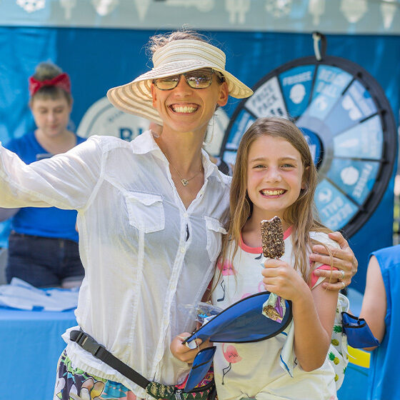 A woman and her daughter embracing and holding up their ice cream while smiling at the camera during ice cream days in le mars.