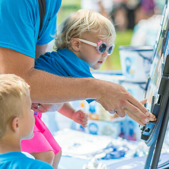 A little boy being held by his father while he spins the prize wheel at the Blue Ribbon Classics booth during Ice Cream Days in Le Mars.
