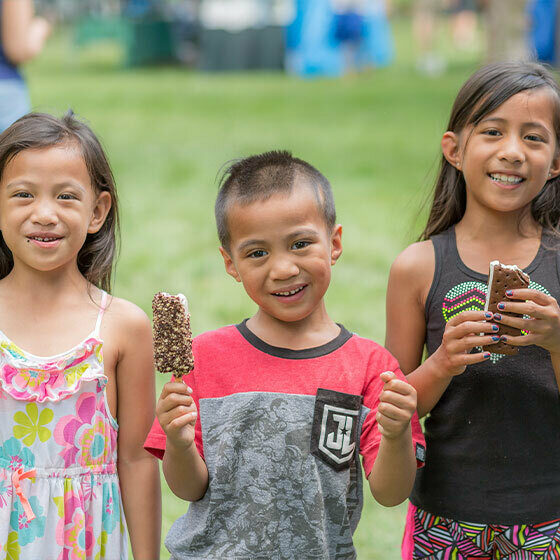 Two little girls and their younger brother eating ice cream and smiling at the camera during Ice Cream Days in Le Mars.